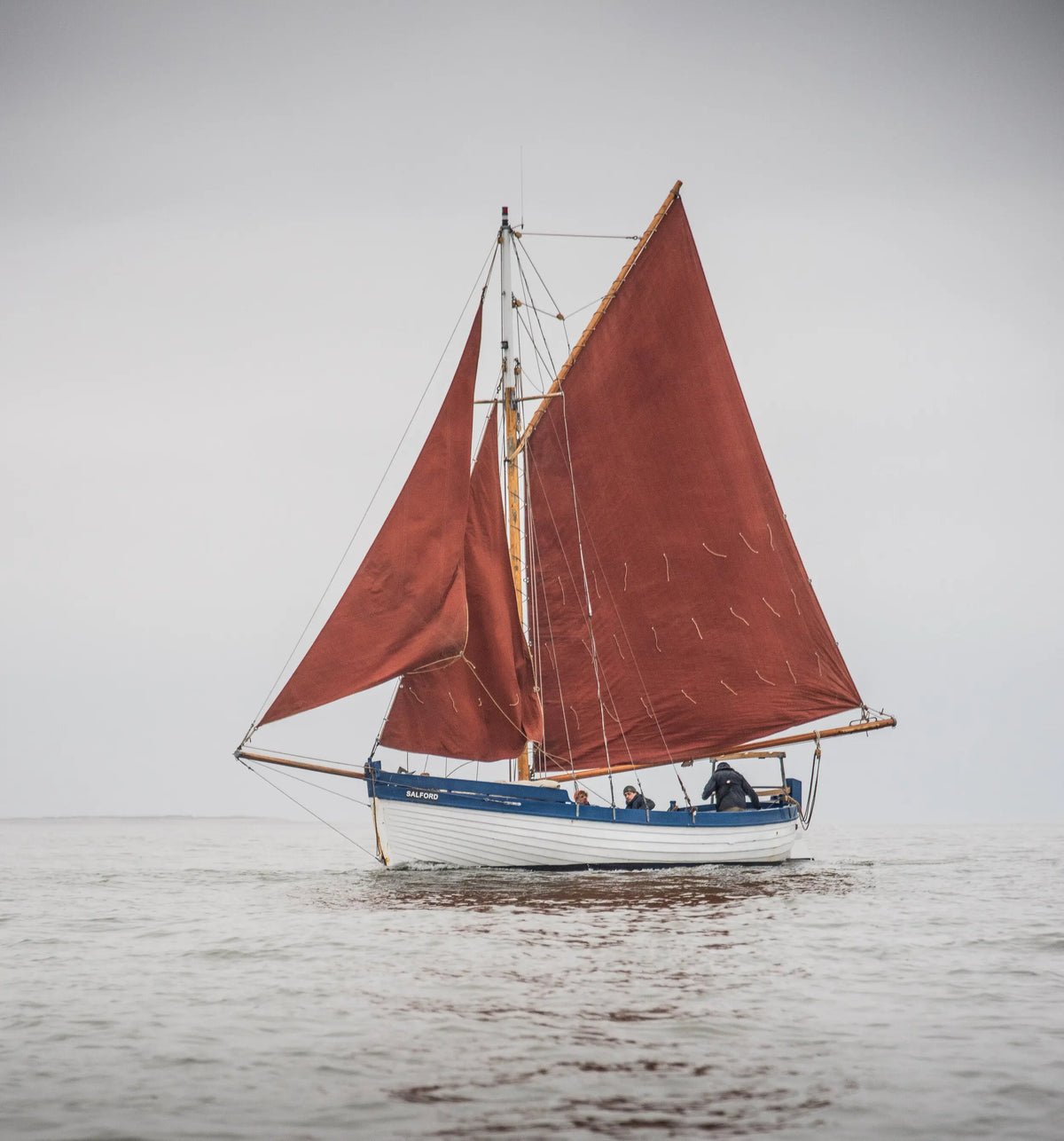 Sailboat with red sails on a calm body of water under a gray sky